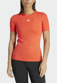 Camiseta atlética de manga corta en un vibrante color naranja, hecha de un tejido elástico y que absorbe la humedad. Presenta un pequeño logo blanco en el pecho.