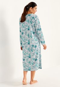 Lång, lätt nattlinne i ljusgrått med turkosa blommönster, långa ärmar och rundad halsringning, som når mitt på vaden.