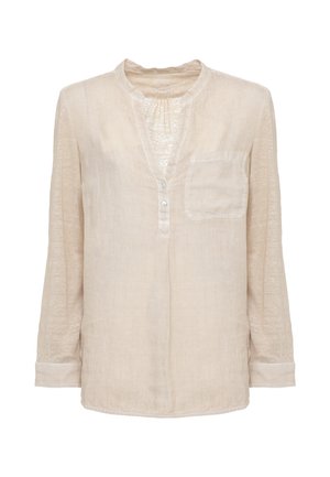 Donna che indossa una camicetta beige a maniche lunghe e pantaloni a gamba larga abbinati, tiene una borsa intrecciata e indossa sandali con zeppa.