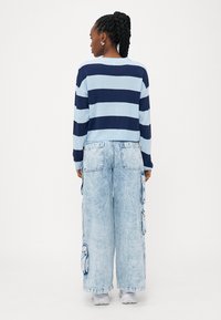 Pullover listrado em azul e azul claro com mangas longas, combinado com jeans cargo de perna larga de lavagem clara, apresentando bolsos e um ajuste descontraído.