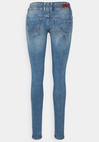 Jeans ajustados de mezclilla en azul claro, con bolsillos traseros que tienen un detalle de costura curvada y una etiqueta de cuero en la cinturilla.