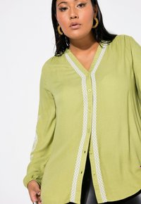 Camicia verde lime con bottoni, caratterizzata da un collo a V, dettagli ricamati bianchi e maniche lunghe con una vestibilità morbida.