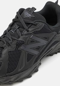 Black athletic shoe featuring mesh material, sleek design, textured surfaces, and prominent rubber outsole with multi-directional lugs.