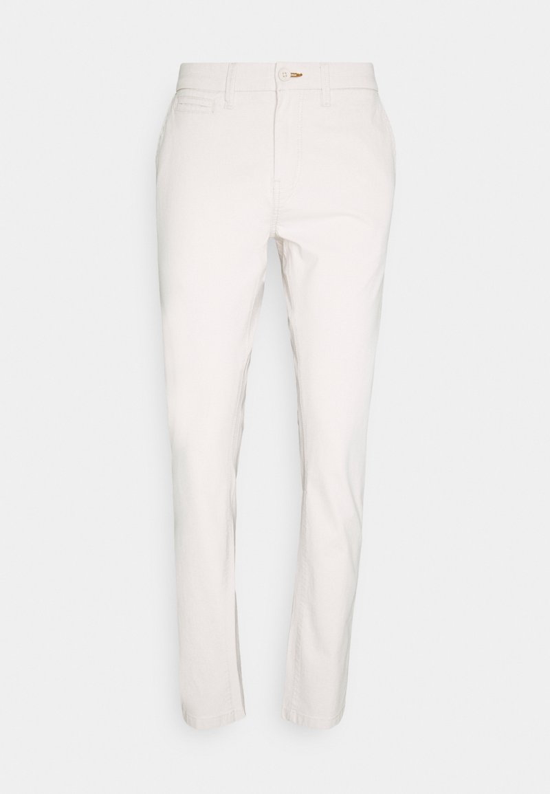 Pantalones ajustados de color blanco roto con cierre de botón y cremallera, trabillas para cinturón y bolsillos laterales y para monedas, exhibidos sobre un fondo liso.