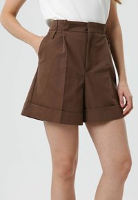 Shorts marron taille haute avec jambes larges, plis à l'avant et revers rabattus. Dotés de poches latérales et d'une fermeture éclair dissimulée.