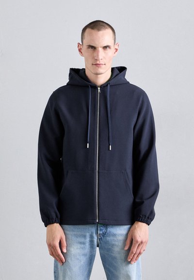 Marineblaue Zip-Hoodie mit Kordelzug, elastischen Bündchen und Fronttaschen, aus einem glatten, leichten Stoff gefertigt.