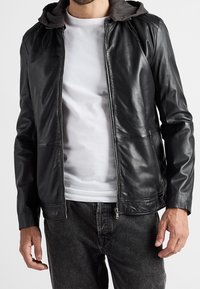 Černá kožená bunda se šedou kapucí, předním zipem a dvěma bočními kapsami. Nositelná přes bílé tričko a doplněná tmavými džínami.