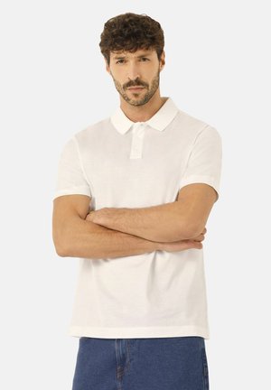 Camisa polo blanca de manga corta con cuello clásico, que presenta una abertura con botones y un corte relajado, combinada con pantalones cortos de mezclilla azules.