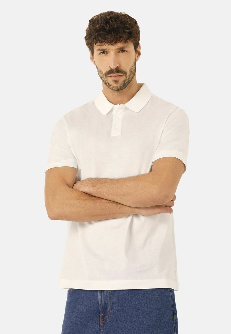 Vit kortärmad polo-shirt med klassisk krage, som har en knappslå och en avslappnad passform, ihop med blå denimshorts.