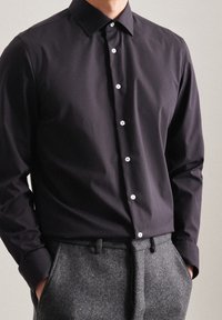 Camisa negra de manga larga con cuello abotonado y botones blancos, combinada con pantalones grises de talle alto y textura.