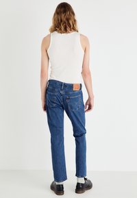 Blå denim jeans med rett benpassform, en beige lærlapp bak på livet, og diskret søm på lommene. Kombinert med en hvit tanktop.