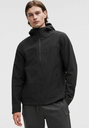 Czarna kurtka typu softshell z kapturem, z zamkiem błyskawicznym z przodu oraz kieszeniami, o gładkiej fakturze i minimalistycznym designie, odpowiednia do aktywności na świeżym powietrzu.