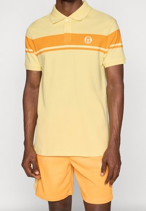 Gul pikétröja med orangea ränder, korta ärmar, tvåknappsknäppning och en logotyp på bröstet. Matchas med matchande gula shorts.