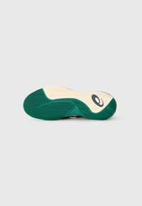 Semelle de chaussure de sport en caoutchouc vert et crème, avec des motifs en zigzag pour une meilleure adhérence, et un détail de logo en couleur sombre.