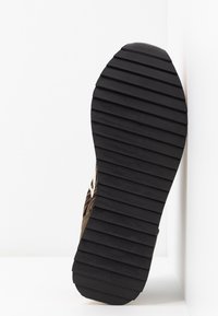 Semelle de chaussure avec larges crampons noirs horizontaux espacés régulièrement, inclinée sur un fond blanc.