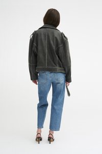 Veste en cuir noir avec des détails de couture visibles, associée à un jean droit bleu clair et des sandales à talons noires.