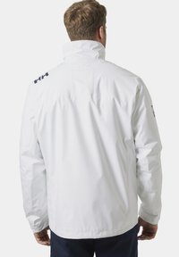 Chaqueta impermeable blanca con collar alto, que presenta un logo en el hombro, puños elásticos y un corte holgado para mayor comodidad.