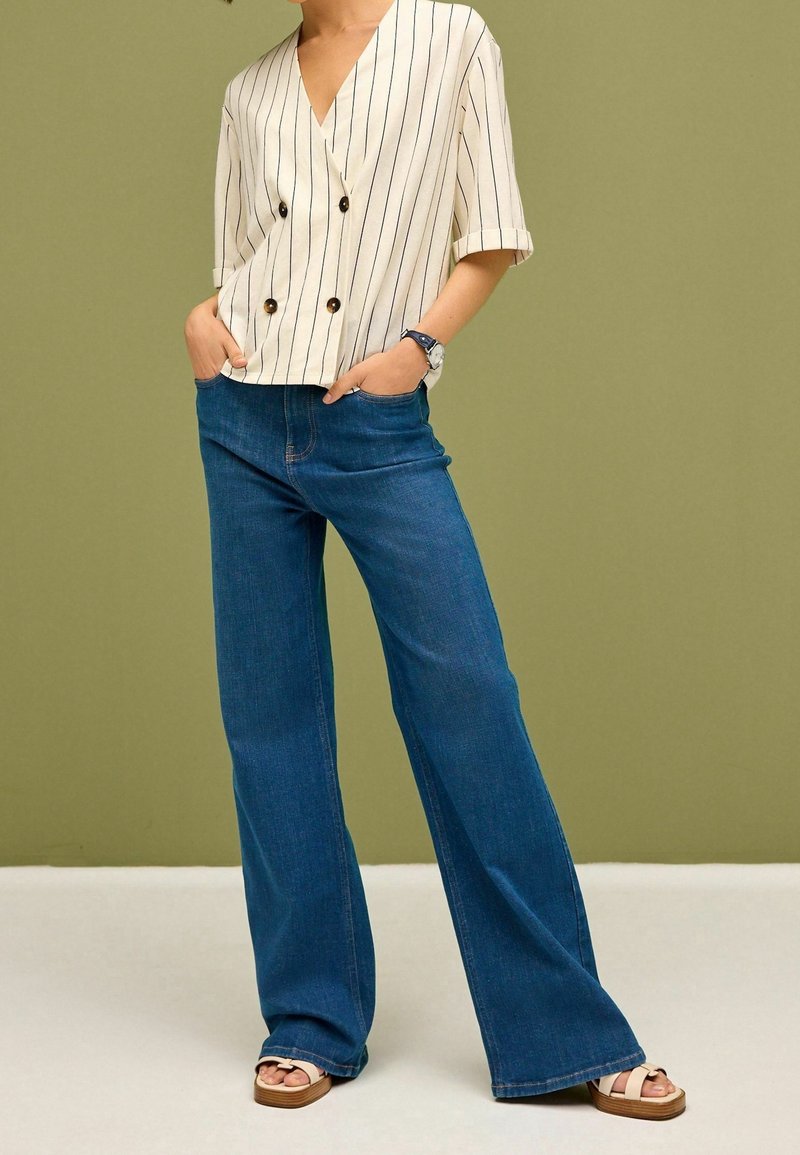 Kerman raidoitu lyhythihainen pusero, jossa on tupla-napit, yhdistetty sinisiin levennettyihin farkkuihin. Jalkineina ruskeat alustasaappaat, joissa on strapsit.