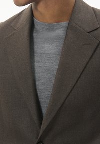 Brown textured blazer layered over a light gray, ribbed sweater. Features a notched lapel and a subtle stitching detail on the blazer.