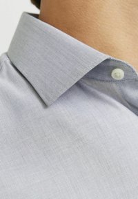 Camicia azzurro chiaro con texture a quadretti, colletto a punta e un solo bottone al colletto. Motivi fini molto evidenti su tutta la superficie.