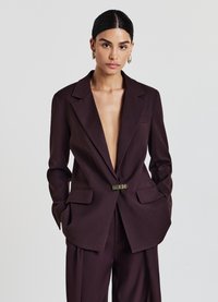 Blazer tailored borgogna con rever a punta, apertura frontale, due tasche anteriori e un gancio metallico. Realizzato in materiale liscio e strutturato.