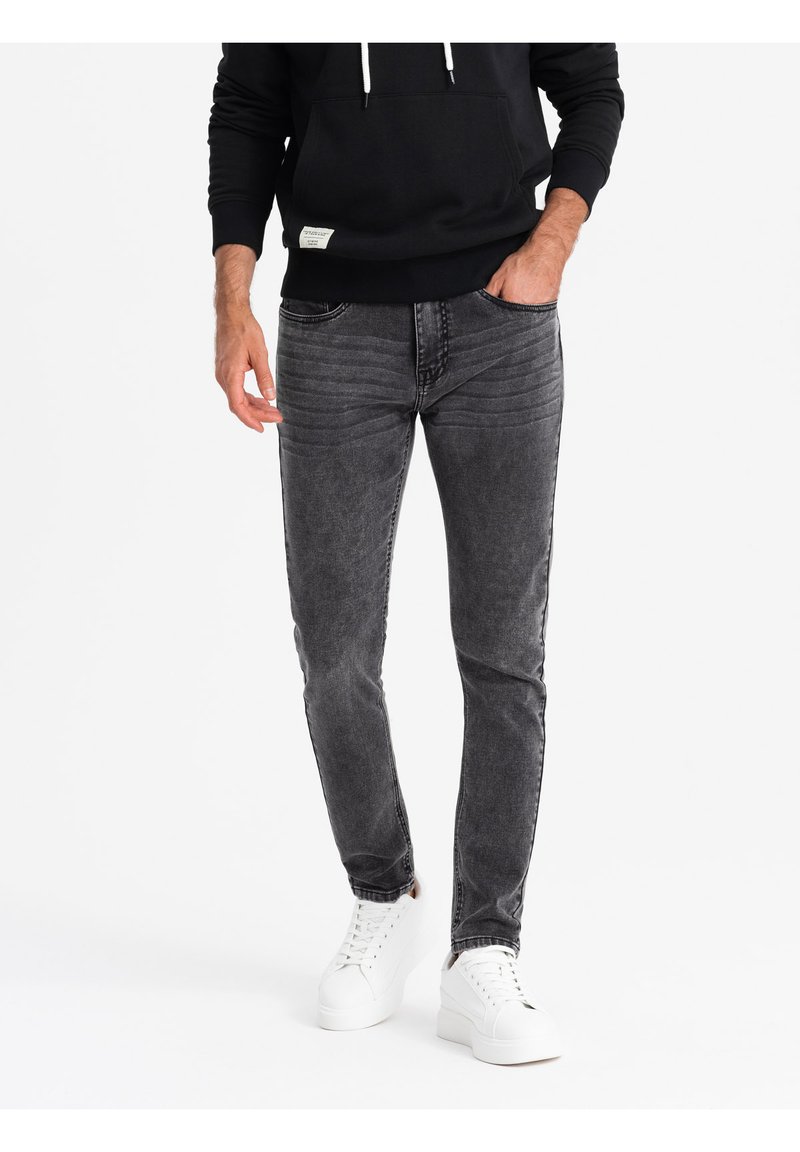 Jeans de mezclilla gris ajustados con desgastado sutil, cinco bolsillos y costuras en contraste, combinados con zapatillas blancas y una sudadera negra con capucha.