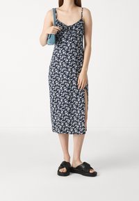 Blommig midiklänning i marinblått med vita blommor, med tunna axelremmar, samlad fram och sidofrackar. Bärs med svarta plattformssandaler.