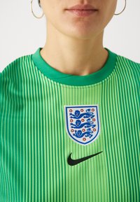 Zaļš svītrots sporta krekls ar apaļu kakla izgriezumu, kas rotāts ar Anglijas ģerboni un melno Nike logo uz krūtīm.