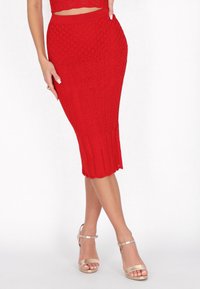Roter gestrickter Midikleid mit strukturiertem Kabeldesign, geripptem Saum und figurbetontem Schnitt. Kombiniert mit metallischen Riemchenheels.