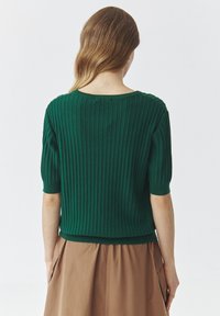 Groen geribbeld gebreid sweater met korte mouwen, voorzien van een ronde hals en een aansluitende onderrand, gecombineerd met een beige rok.