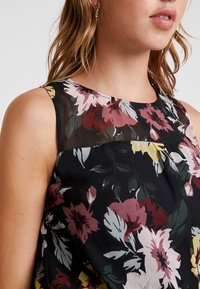 Floral sleeveless top featuring a sheer black panel, with red, pink, and yellow flowers on a black background. Lightweight fabric with a subtle sheen.