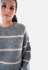 Grijze gebreide trui met witte horizontale strepen, met een ronde hals en gestructureerd garen, gefotografeerd tegen een effen achtergrond.