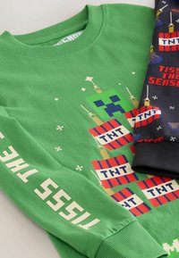 Green sweatshirt featuring a pixelated character design, sword graphics, and colorful 'TNT' blocks. Includes white text along the sleeve.