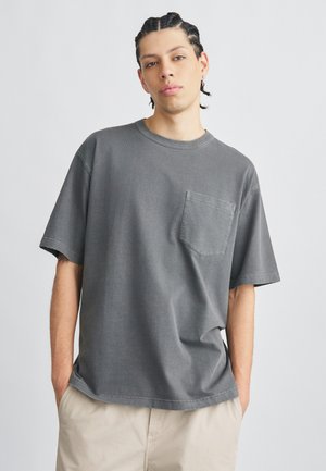 T-shirt grigia in cotone con maniche corte e taschino sul petto. Presenta una vestibilità morbida e un design a girocollo. Finitura testurizzata e scolorita.