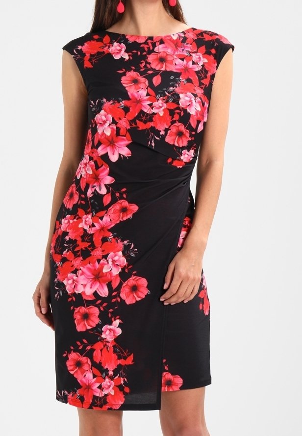 Robe noire sans manches avec motifs floraux rouges et roses, taille cintrée, longueur genou, portée avec des boucles d'oreilles pendantes rouges.