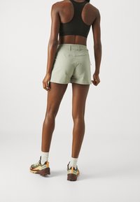 Ljusgröna shorts med en figurnära design, tillverkade av ett slätt material, kombinerade med flerfärgade trailskor och vita strumpor.