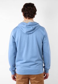 Un hoodie bleu clair en matériau doux, avec une capuche à cordon de serrage et des poignets côtelés, vu de l'arrière. Design décontracté, sans embellissement.