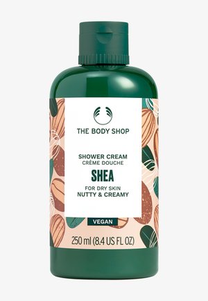 Grüne Flasche der Body Shop Shea Duschcreme für trockene Haut, nussig und cremig, 250 ml, mit veganem Label und illustriertem Nussmuster.