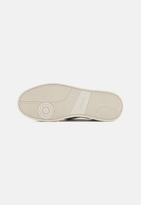 White rubber sneaker sole with textured grip pattern and circular accent. Features logo marking and streamlined design.