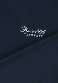 Granatowy materiał o gładkiej teksturze z białym wyszywanym napisem: "Prosto 1999 TEAMWEAR". Projekt stawia na czyste linie i minimalistyczny wygląd.