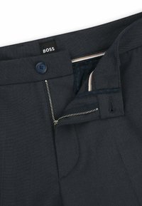 Dark gray trousers featuring a BOSS label, blue button, metal zipper fly, and subtle textured fabric with internal patterned lining.