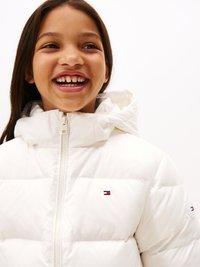 Balta pūkaina jaka ar rāvējslēdzēju priekšpusē un divām emblēmām uz krūtīm un piedurknēm. Tai ir augsts kakls un quilted tekstūra.
