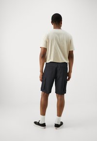 Beige T-Shirt mit kurzen Ärmeln und dunklen Cargo-Shorts mit mehreren Taschen. Die Shorts haben eine gerade Passform und sind aus leichtem Stoff gefertigt.