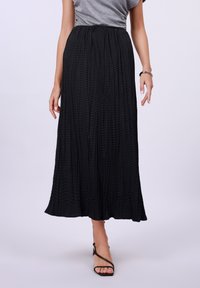 Gonna maxi nera a pieghe con vita elasticizzata, tessuto testurizzato, forma fluida e leggero svaso all'orlo, abbinata a sandali con cinturini.