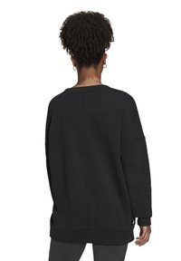 Sudadera negra de gran tamaño con cuello redondo, hombros caídos y mangas largas. Textura suave con un sutil detalle de costura en la parte trasera.
