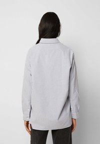 Stribet button-up skjorte i bomuldsblanding med lange ærmer, krave og løs pasform. Farverne inkluderer hvid og marineblå.