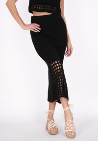 Černý pletený crop top a odpovídající sukni s vysokým pasem a detailem otevřeného vzoru. V kombinaci se světle béžovými sandály na podpatku se pásky.