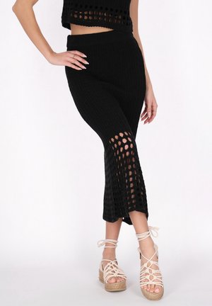 Zwart gebreid crop top en bijpassende hoge taille rok met openholpatroon. Gecombineerd met lichtbeige gekruiste wedges.