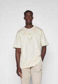 Beige puuvillane T-särk lühikeste varrukatega, mille rindkereosas on toon-toonis logo disain. Pehme tekstuur ja lõdvestunud istuvus.