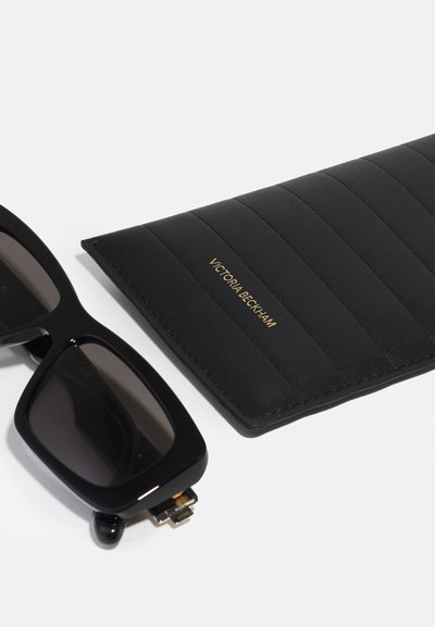 Occhiali da sole neri oversize con montatura spessa, abbinati a un astuccio nero trapuntato. L'astuccio presenta la scritta dorata "Victoria Beckham".